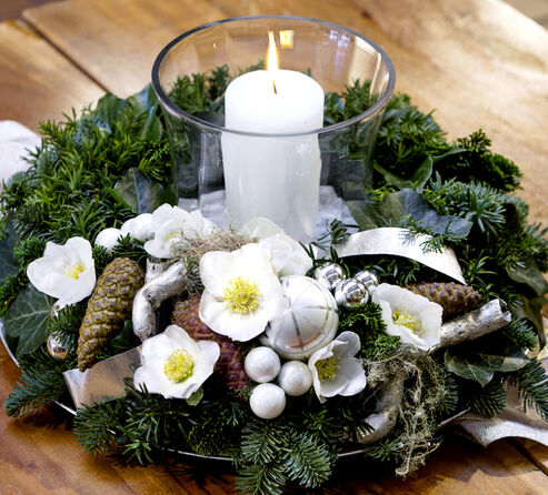 Enkele bloemen in een krans van dennentakken versierd met kerstballen, dennenappels en korstmossen